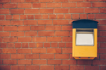 Empty yellow blue post box on old red brick wall with empty space on left
