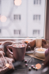 Mug of hot cocoa or hot chocolate with marshmallow on windowsill