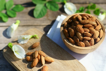 Almond nut in wooden bowl on wood table with green leaf background, copy space