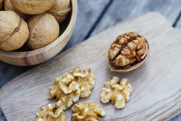 Walnut nut in wooden bowl on wood table with green leaf background, copy space