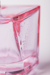 White and pink background. Glass with water drops. Perfume