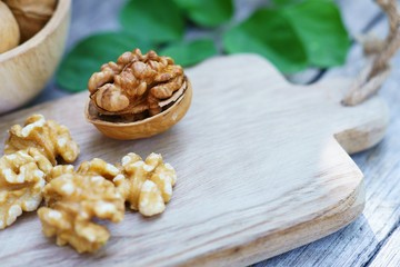 Walnut nut in wooden bowl on wood table with green leaf background, copy space
