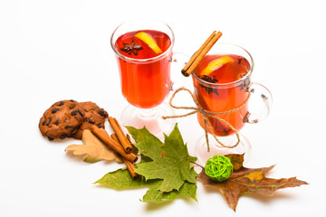 Glasses with mulled wine or hot drink near autumn leaves and cookies on white background, close up. Autumn drink concept. Mulled wine or hot beverage in wineglasses with cinnamon sticks