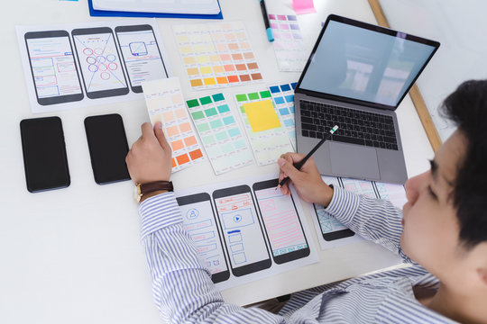 Creative ux designer designing screens for mobile responsive website development with UI/UX. Developing wireframe sketch layout design mockup on smartphone screen.