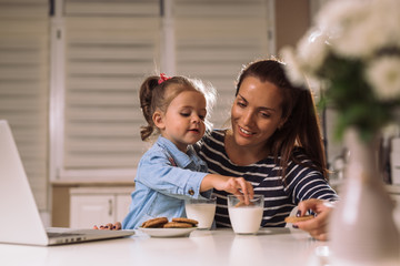 Mother and daughter eating cookies and milk at home - obrazy, fototapety, plakaty