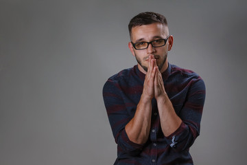 Man praying. Attractive male wearing checkered shirt and glasses while stands on a dark gray background