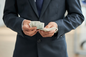 Close-up of businessman in black suit counting dollar currencies