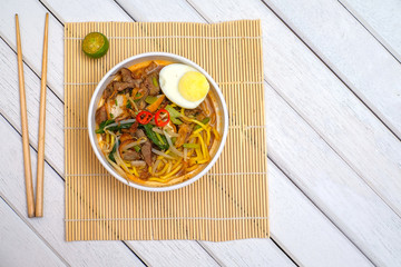 Malay Mee Rebus in the bowl  with chopsticks on white table This dish is made of noodles ,vegetable,egg with a spicy .