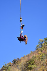 Bungee jumping. Beautiful young girl with long ponytail hanging on a cord high in the blue sky