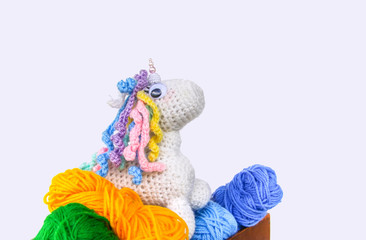 Handmade crocheted unicorn toy and yarn in a wooden box on white background.