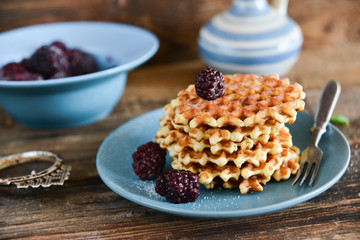 Round waffles with fresh blackberries and whipped cream, on natural wooden background in rustic style