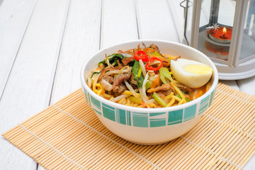 Malay Mee Rebus in the bowl  with chopsticks on white table This dish is made of noodles ,vegetable,egg with a spicy .