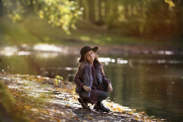 Fototapeta na wymiar Beauty kid girl with long hair sitting near the river at the sunny evening