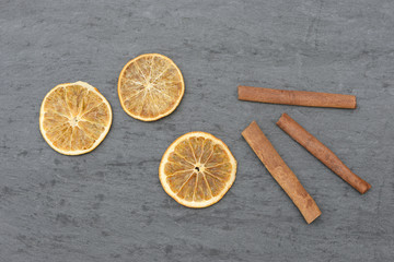 cinnamon sticks and orangen slices lying on black slate