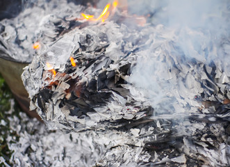 Paper burning on green summer grass outdoors. Grey ash.