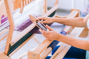 Obraz premium Women's hands weave a lilac canvas of thread on a weaving machine