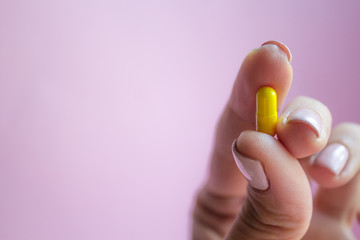 woman hand holding yellow pill capsule on pink background, medication concept with copy space