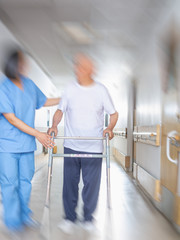 Asian doctor helping elder man with walker in hospital hallway