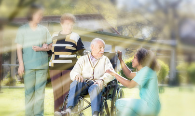 Two female doctors helping elderly man and woman with physical disability ih rehab facility garden