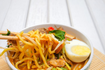 Malay Mee Rebus in the bowl  with chopsticks on white table This dish is made of noodles ,vegetable,egg with a spicy .