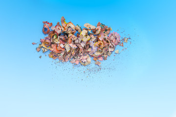 Wooden pencil shavings and colorful crumbs of graphite from sharpener on soft pastel paper background. Top view. Design elements for poster, banner, cards