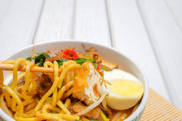 Malay Mee Rebus in the bowl  with chopsticks on white table This dish is made of noodles ,vegetable,egg with a spicy .