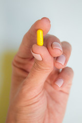 woman hand holding yellow pill capsule on light blue background, medication concept
