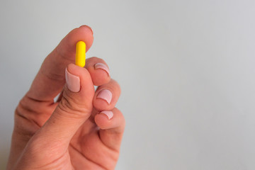 woman hand holding yellow pill capsule on light blue background, medication concept with copy space