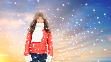 people, season and leisure concept - happy woman in winter fur hat outdoors over sky background and snow