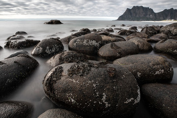 Fototapeta na wymiar Long exposure of waves washing over rocks in Uttakleiv beach on a dark and cloudy day. Lofoten, Norway.