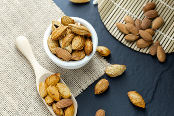 Almonds in a black bowl against dark rustic wooden background