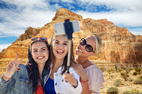 tourism, travel and technology concept - group of smiling women of friends taking pictyre by smartphone on selfie stick over grand canyon national park background
