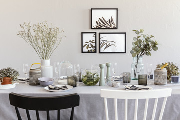 Black and white chair at table with tableware in grey dining room interior with posters. Real photo