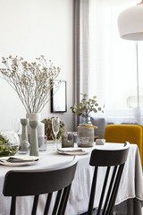 Black chairs at table with plants and tableware in bright dining room interior with window. Real...