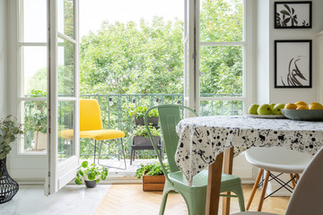 Relaxing space on a balcony with a vibrant yellow chair and homegrown plants and herbs outside a scandinavian dining room interior - obrazy, fototapety, plakaty