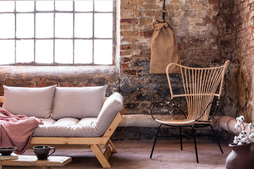 Armchair next to grey sofa with cushions in industrial interior with window and red brick wall....