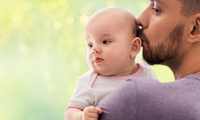 family, parenthood and people concept - close up of father kissing little baby daughter over festive lights background