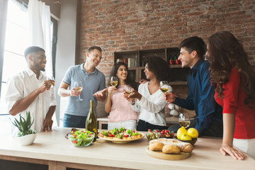 Excited friends drinking and chatting in kitchen