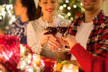 holidays and celebration concept - close up of happy friends having christmas dinner at home, drinking red wine and clinking glasses