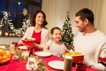 holidays, family and celebration concept - happy mother, father and little daughter having christmas dinner at home