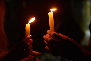 hands holding a burning candle in dark