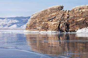 Fototapeta na wymiar Baikal Lake in February. The rocky island of Ogoy is reflected in the mirror smooth blue ice