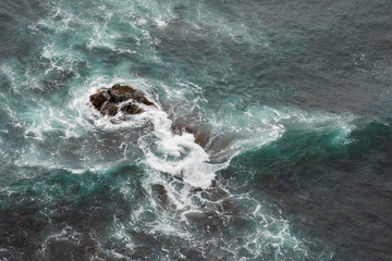 White ocean waves crashing over coastal sea rocks in summer.