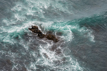 White ocean waves crashing over coastal sea rocks in summer.
