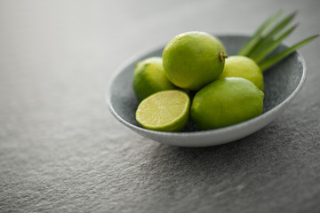 food, healthy eating and vegetarian concept - close up of limes in bowl on slate table top