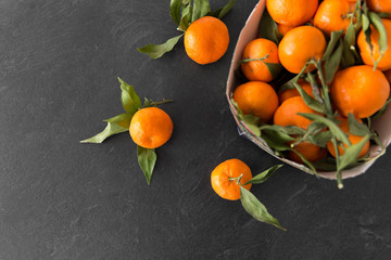 food, healthy eating and vegetarian concept - close up of whole mandarins with leaves on slate table top