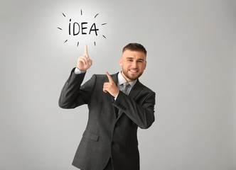 Handsome businessman pointing at word IDEA on grey background