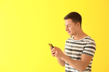 Young man with mobile phone on color background