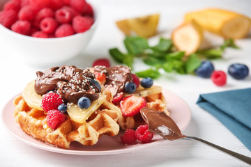 Delicious waffles with berries, kiwi slices and chocolate sauce on plate