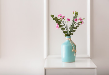 Vase with beautiful pink flowers on dresser near white wall